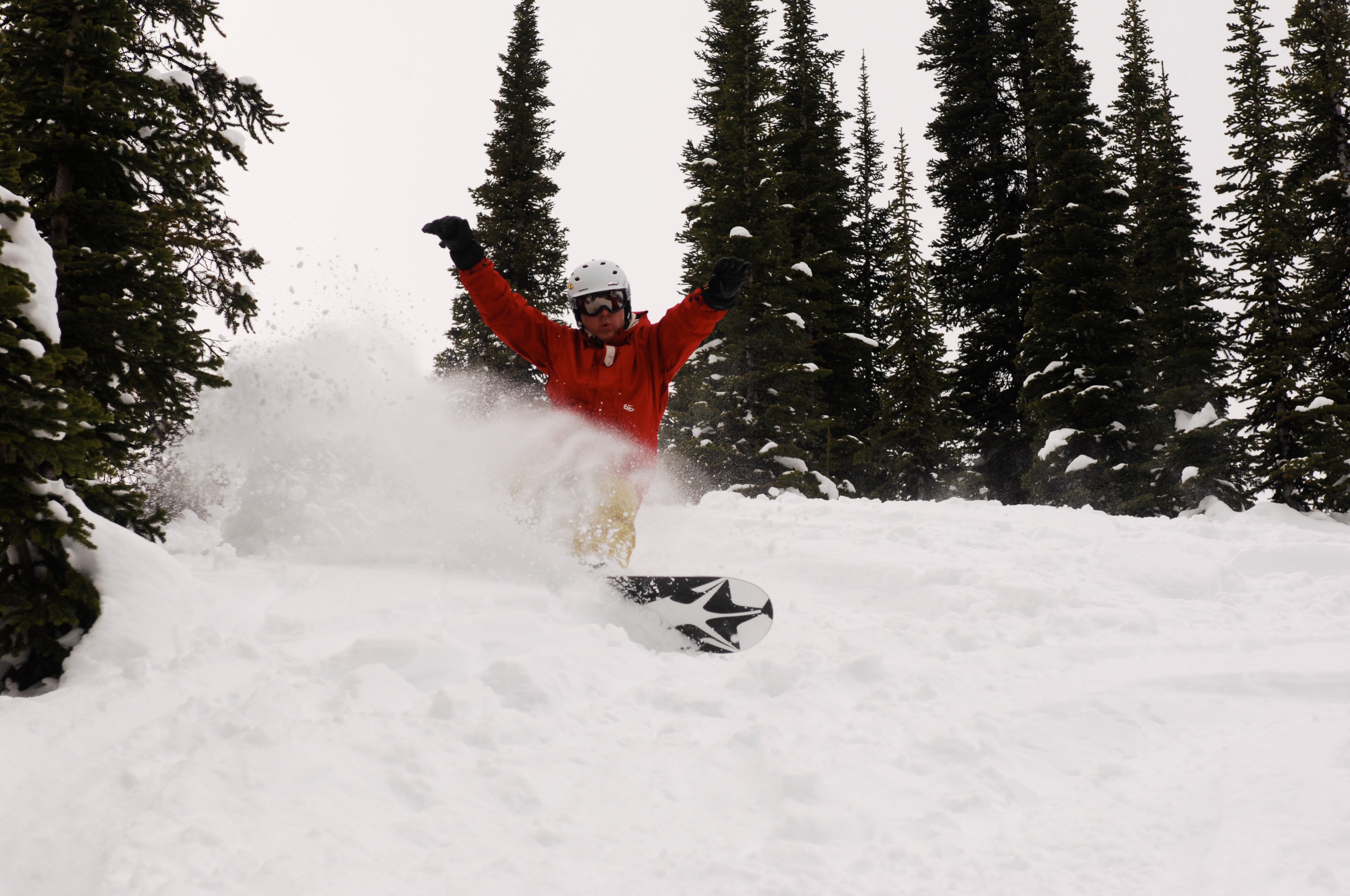 Person in a red jacket snowboarding through deep snow with trees in the background