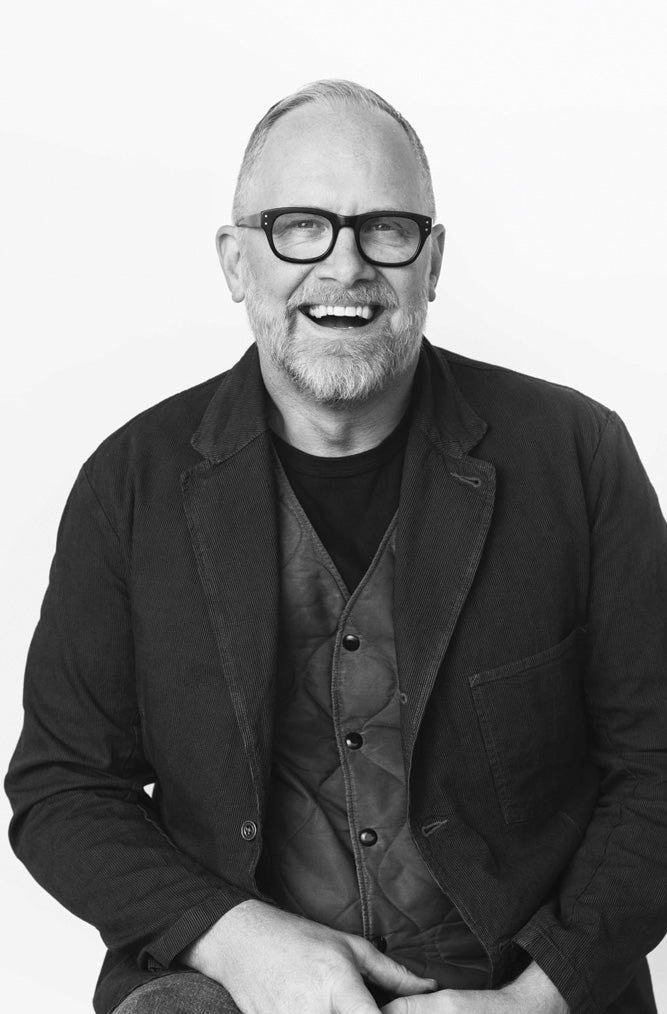 Black and white portrait of a man wearing glasses and a jacket.